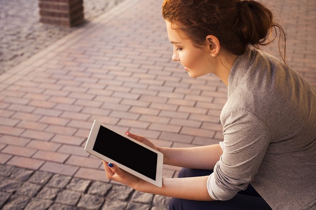 A photo of a woman sitting on a street holding a tablet.